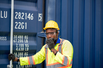 Worker man in protective safety jumpsuit uniform with yellow hardhat and use  Walkie Talkie check container at cargo shipping warehouse. transportation import,export logistic industrial service