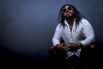 Man with dreadlocks squatting holding a drink.