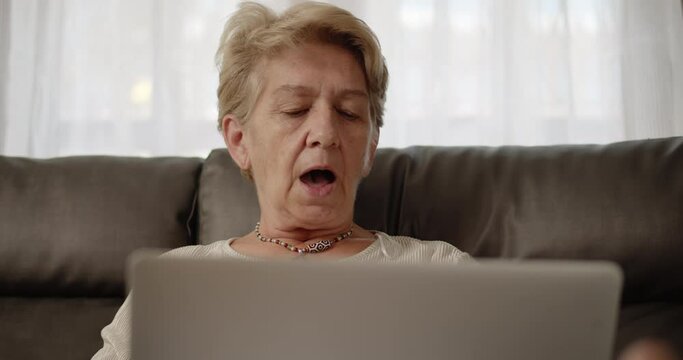 Older women have to work from home with online training meetings on a laptop and she was in a comfortable position leaning on the sofa at her home alone.	