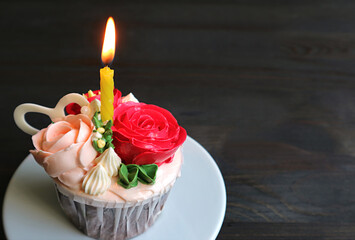 Decorative birthday cupcake decorated with rose bouquet shaped frosting with a shining candle