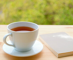 Cup of hot tea on the outdoor table with blurry foliage in background