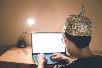 Conspiracy theory concept: young man with aluminum cap searching the internet, sitting lonely in...