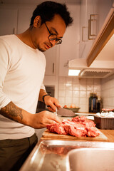 person preparing food in kitchen, Asian man cutting meat with knife on a wooden 
cutting board