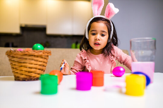 hispanic happy baby painting eggs in kitchen in modern home