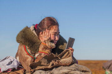 A young girl, in the national winter clothes of the northern inhabitants of the tundra, takes a...