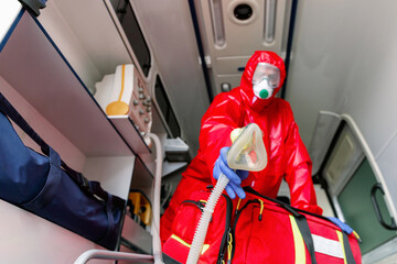 Naklejka premium Male paramedic with face mask helping a patient with respirator in ambulance during pandemic. A portrait of paramedic sitting in an ambulance car.