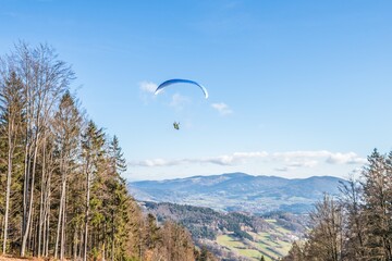 Fliegender Hobby Gleitschirm Flieger an einem Berghang mit professioneller Ausrüstung im Herbst mit Aussicht auf Berge und Alpen im Hintergrund, Deutschland