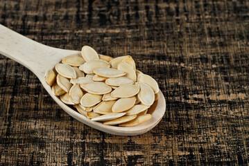Pumpkin seeds in a wooden spoon on a yellow bamboo board. Nuts on a brown table.