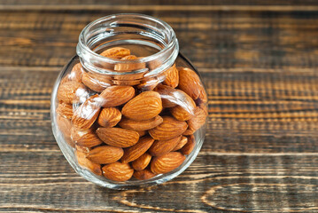 Almonds in a glass transparent jar. Nuts on an old shabby board. Jar on a brown wooden table close up.