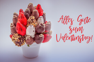 Happy valentine's day greeting card in German that reads Alles Gute zum Valentinstag with red lettering; A bundle of edible flowers, arrangement of strawberries covered in chocolate isolated on white