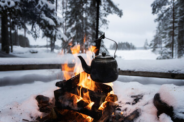 Kettle over an open fire in winter. Boiling kettle on firewood. Open fire cooking. Lifestyle, camping. Blurred background. Snowy weather.  - 407894528