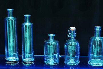 Glass bottles of different sizes and shapes on a dark background. Transparent containers for bottling wine and spirits