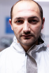 Obraz premium Close up of exhausted pediatric dentist man marks on face because of protection mask. Portrait of tired stomatologist wearing coronavirus ppe suit looking at camera.