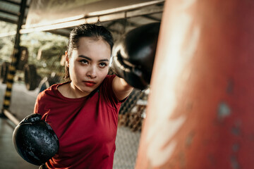 woman boxer fighter doing exercise hitting punching bag with copyspace at boxing camp