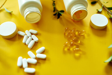 Flat lay of pills, fish oil, vitamins with green leavws on yellow background