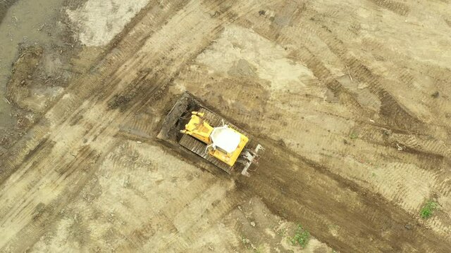 Above top view bulldozer is pushing muddy ground, leveling, equates sediment.