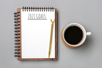 Fototapeta na wymiar open notepad with text 2021 goals, cup of coffee, golden pen on gray background, spiral notebook on table Business, planning, check list, education concept Top view Flat lay