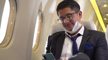 businessman passengers incorrect wearing protective medical face mask on chin using smartphone sitting in airplane. wrong new normal of traveling by plane during the coronavirus pandemic or Covid-19 - Powered by Adobe