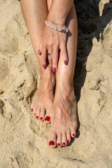 Woman legs with red pedicure relaxing on the sand. The hand strokes the leg. Summer beach