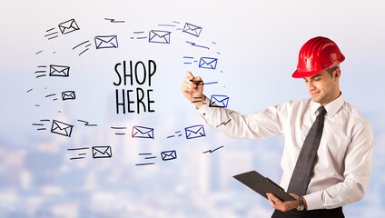Handsome businessman with helmet drawing SHOP HERE inscription, contruction sale concept