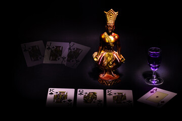 Still life in a low key, fortune telling on cards in front of a statuette of the leader of Hawaii with a glass of potion.