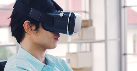 Asian man wearing virtual reality glasses experiencing innovative technology in the modern home, handsome man playing game using VR glasses on a sunny day.