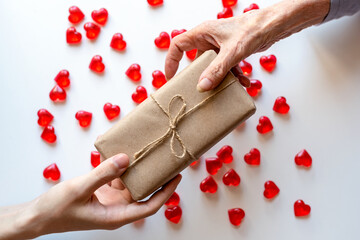 Hands of a young man give a gift to an elderly woman. Small stones in the shape of a heart with a...