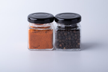 Green chili peppers, chili peppers, and pimento in glass bottles on white background.