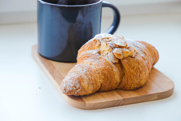 Croissant with almonds and ceramic cup on white. Morning light. Breakfast for one.