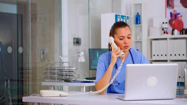 Medical staff talking with patient on phone from hospital about diagnosis, male nurse working in background. Healthcare physician, receptionist doctor assistant helping with telehealth communication