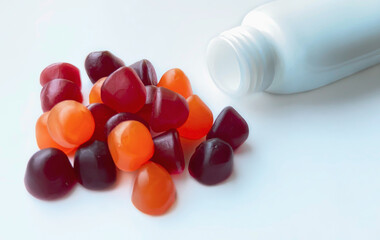 Group of red, orange and purple multivitamin gummies with the bottle isolated on white background....