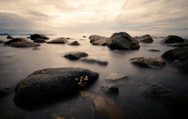 Fototapeta na wymiar calm sea with stones during sunrise or sunset, long exposure shot of rocks in the smooth water