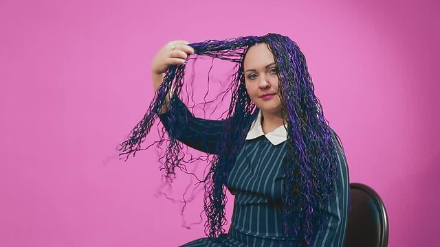 Stylish Jewish brunette with blue afro braids on a chair shakes her hair effectively