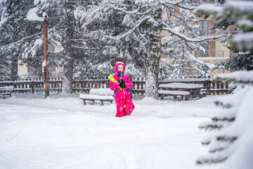 Funny little girl having fun in beautiful winter park during snowfall. Child playing with snow in winter. Kids play and jump in snowy forest