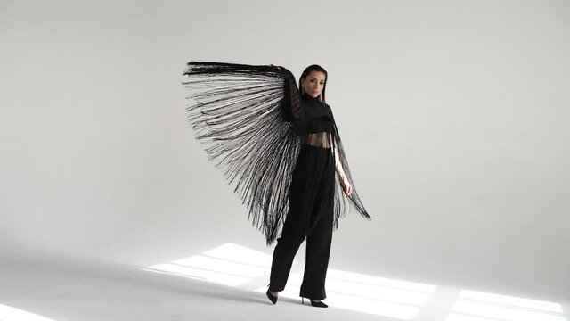 girl on a white background in black clothes in a suit with a long fringe turns in slow motion, from which the fringe begins to cast beautifully