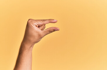 Arm and hand of caucasian man over yellow isolated background picking and taking invisible thing, holding object with fingers showing space