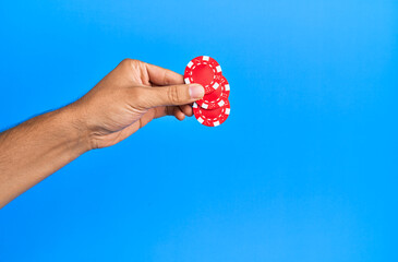 Hand of hispanic man holding casino chips over isolated blue background.