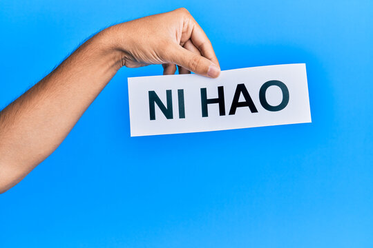 Hand of hispanic man holding chinese greeting ni hao word paper over isolated blue background.