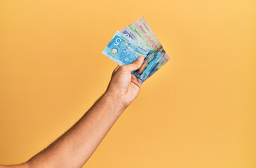 Hand of hispanic man holding canadian dollars over isolated yellow background.