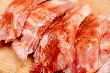 raw pork ribs sprinkle with salt, black pepper and paprika on a wooden cutting board. cooking meat at home. Cook.