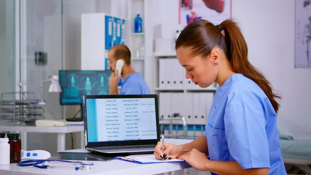 Doctor assistant checking list diagnosed of patients, writing on clipboard with x-ray and medical equipment around. Physician working in hospital making appointments and analysing patient registration