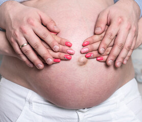 Close-up photo of a naked pregnant tummy. Men's hands hug the belly of their pregnant wife.