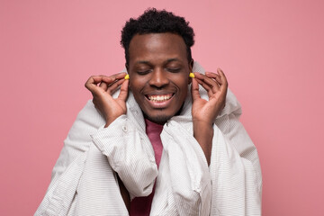 African young man holding a yellow earplug trying to sleep having insomnia. Studio shot