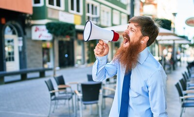 Young redhead businessman with angry expression. Screaming using megaphone at street of city.