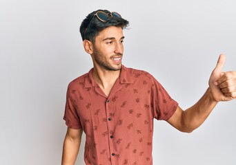 Young handsome man wearing casual summer clothes looking proud, smiling doing thumbs up gesture to the side