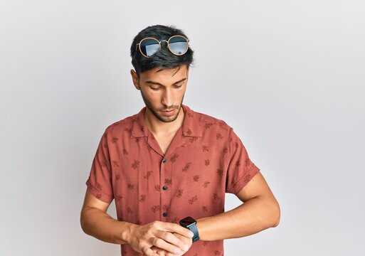 Young handsome man wearing casual summer clothes checking the time on wrist watch, relaxed and confident