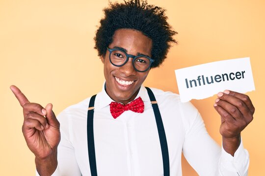Handsome african american man with afro hair holding paper with influencer text smiling happy pointing with hand and finger to the side