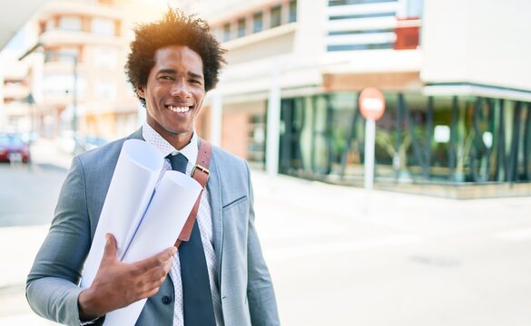 Young handsome african american architect man smiling happy. Standing with smile on face holding blueprints walking at town street.