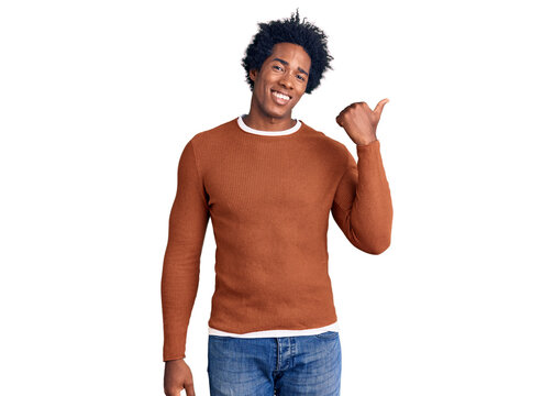 Handsome african american man with afro hair wearing casual clothes smiling with happy face looking and pointing to the side with thumb up.