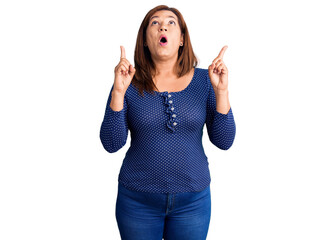 Middle age latin woman wearing casual clothes amazed and surprised looking up and pointing with fingers and raised arms.